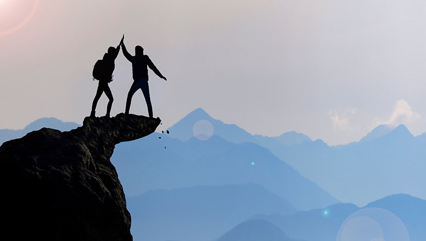 Zwei Personen erreichen gemeinsam einen Berggipfel.